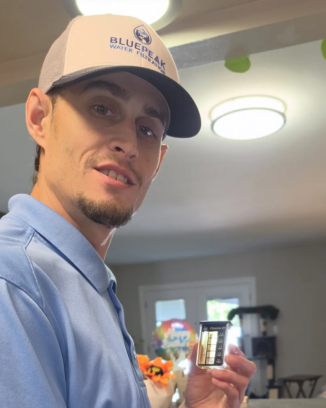 Branden, the owner of BluePeak Water Filtration, holding a water test vial at a kitchen sink.